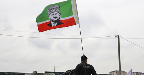 Сотрудник чеченского СОБРа с флагом республики, на который наложен портрет Ахмата Кадырова. 9 мая 2015 года, Грозный. Фото Магомеда Магомедова для "Кавказского узла" Сотрудник чеченского СОБРа с флагом республики, на который наложен портрет Ахмата Кадырова. 9 мая 2015 года, Грозный. Фото Магомеда Магомедова для "Кавказского узла"